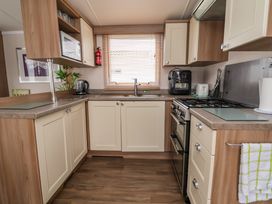 A kitchen with cream cabinets a microwave kettle coffee machine toaster gas stove and a window with blinds at Hazel Park 11 HP11 in Rhyl