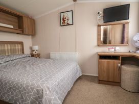 A bedroom with a bed covered in patterned bedding a wooden desk with a mirror wall mounted tv and a fan at Hazel Park 11 HP11 in Rhyl