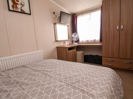 A bedroom with a bed, wardrobe, desk, mirror, fan, and window at Hazel Park 11 HP11 in Rhyl