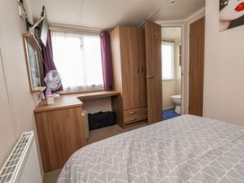 A bedroom with a bed a wooden wardrobe a desk with a fan and a window with purple curtains at Hazel Park 11 HP11 Rhyl