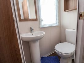 A small bathroom with a white pedestal sink mirror window with blinds white toilet and blue bath mat at Hazel Park 11 HP11 in Rhyl