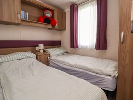 A bedroom with two single beds a bedside table and lamp a window with curtains and overhead storage cabinets at Hazel Park 11 HP11 in Rhyl