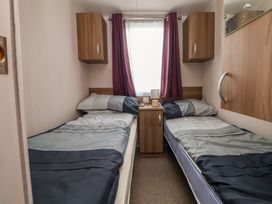 A bedroom with two single beds separated by a wooden nightstand with a lamp and remote control and purple curtains on the window at Hazel Park 11 HP11 in Rhyl
