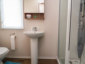 A bathroom with a pedestal sink a shower cubicle a toilet with a toilet paper holder a window with blinds and a blue bath mat at Hazel Park 11 HP11 in Rhyl