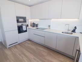 A kitchen with white cabinets built-in appliances a sink and wooden floor at The Links 40 An apartment with spectacular sea views in Porthcawl