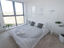 A bedroom with a bed pillows wall art plants and large window at The Links 40 in Porthcawl