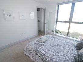A bedroom with a patterned bedspread a closet three framed pictures and a large window at The Links 40 An apartment with spectacular sea views in Porthcawl