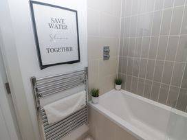 A bathroom with a bathtub two small potted plants a towel rack with a towel and a framed sign at The Links 40 an apartment with spectacular sea views in Porthcawl