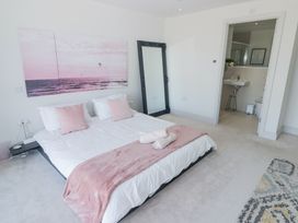 A bedroom with a bed with pink pillows and blanket a standing mirror and an open door to a bathroom at The Links 40 in Porthcawl