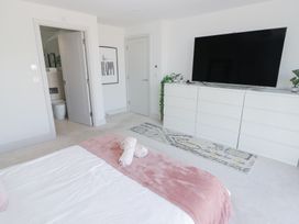 A bedroom with a bed a pink blanket a large white dresser a flat screen TV wall art and two doors at The Links 40 An apartment with spectacular sea views Porthcawl