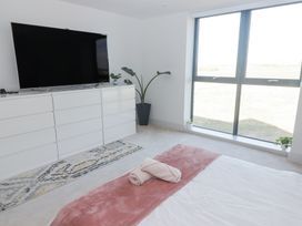 A bedroom with a bed and folded towels on it a large window a white dresser with a television and plants at The Links 40. An apartment with spectacular sea views in Porthcawl