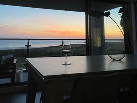 A dining table with a glass of wine and a decorative bowl near a window overlooking the sea at sunset at The Links 40 An apartment with spectacular sea views Porthcawl