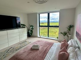 A bedroom with a large window showing grass and hills a bed with pink pillows and blanket a white dresser with a television and plants at The Links 40 An apartment with spectacular sea views Porthcawl