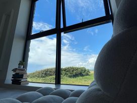A stack of books with a small plant on top next to a large window with a view of greenery and blue sky at The Links 40 in Porthcawl