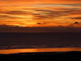 A beach and sea with an orange sunset sky at The Links 40 An apartment with spectacular sea views Porthcawl