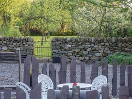 An outdoor patio with white metal chairs and table surrounded by wooden posts with a stone wall and metal gate in the background at Cwt Mochyn in Llanberis