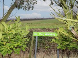 A green dog walking sign on metal posts surrounded by bushes with a field and trees in the background at Charlottes in Holbeach