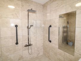 A tiled shower area with two black grab bars a showerhead and a mirror reflecting a mop and bucket at Charlottes in Holbeach