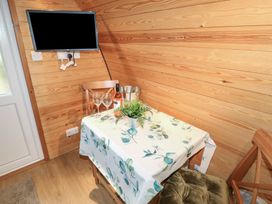 A small dining area with a table covered by a floral tablecloth two wooden chairs a bottle of wine two wine glasses a plant and a wall-mounted television at Charlottes in Holbeach
