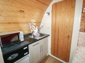 A kitchenette with a microwave, safe, and sink with flowers next to a wooden door at Charlottes in Holbeach