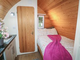 A small bedroom with wooden walls a bed with floral bedding and a pink blanket next to a kitchen sink at Charlottes in Holbeach