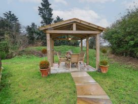A wooden gazebo with outdoor table and chairs on a paved area in a garden at Charlottes in Holbeach