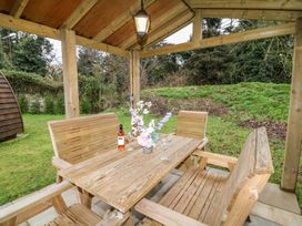 A wooden outdoor seating area with a table, benches, chairs, a bottle of wine, glasses, and a flower arrangement at Charlottes in Holbeach