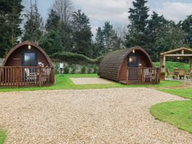 Two wooden camping pods with small porches on grass next to a gravel path and a wooden gazebo with table and chairs at Charlottes in Holbeach