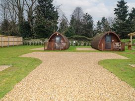 Two wooden pod cabins with porches on grass with a gravel path and trees in the background at Charlottes in Holbeach