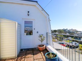 A balcony with potted plants and a white door overlooking a street with cars and buildings at Rosa in Torquay