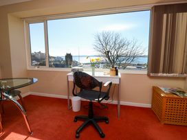 A room with a desk and chair by a large window overlooking a tree and buildings at Rosa in Torquay