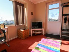A room with a television on a white stand a wooden side table with magazines a colorful striped table a window with vertical blinds and a door with sailboat decals at Rosa in Torquay