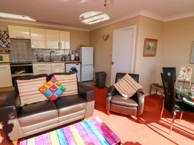 A living area with a brown leather sofa and armchair with striped cushions a colorful coffee table a kitchen with cream cabinets and appliances and a dining table with black chairs at Rosa in Torquay