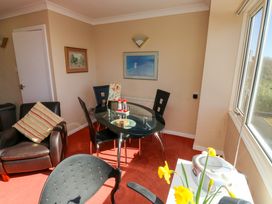 A dining area with a glass table and black chairs a brown armchair with a striped cushion a window with a view and flowers on a table at Rosa in Torquay