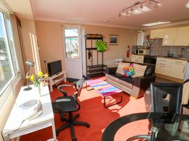 An open plan living room with a desk, office chair, TV, sofa, coffee table, dining table, and kitchen area at Rosa in Torquay