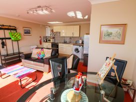 A living room with a brown leather sofa and colorful pillows near a kitchen with white cabinets and appliances at Rosa in Torquay