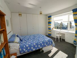 A bedroom with a bed covered with a blue floral bedspread a desk under a window and white wardrobes at Rosa in Torquay