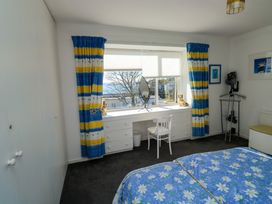 A bedroom with a blue floral bedspread a white desk and chair under a window with blue and yellow curtains at Rosa in Torquay