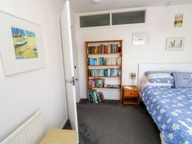 A bedroom with a blue floral bedspread a wooden bookshelf filled with books a small wooden nightstand with a lamp and two framed pictures on the wall at Rosa in Torquay