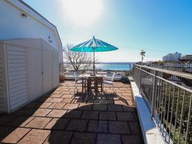 A balcony with a table and four chairs under a blue umbrella overlooking buildings and water at Rosa in Torquay