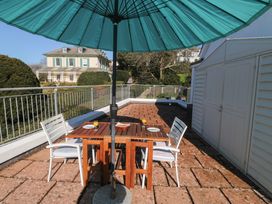 An outdoor patio with a wooden table and four white chairs under a blue umbrella at Rosa in Torquay