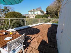 A patio with a wooden table and white chair under a teal umbrella overlooking a white house with green shutters at Rosa in Torquay