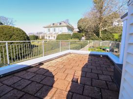 A paved outdoor terrace with metal railing overlooking a large house and garden at Rosa in Torquay