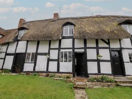 A thatched roof cottage with black timber framing windows flower beds and lawn at Church View in Welford-On-Avon