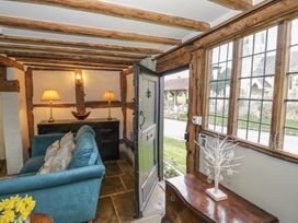 An entrance area with wooden beams a blue sofa a black cabinet with two lamps and a wooden door open to a garden at Church View in Welford-On-Avon