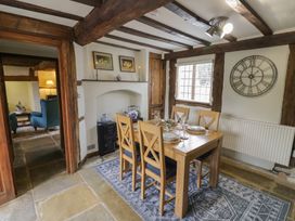 A dining room with a wooden table and four chairs on a rug with a window and large wall clock at Church View in Welford-On-Avon