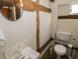 A small bathroom with a toilet a sink a round mirror and exposed wooden beams at Church View in Welford-On-Avon