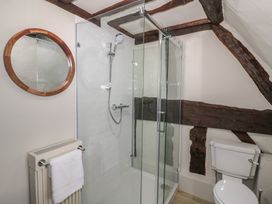 A bathroom with a glass shower enclosure a toilet a round wall mirror and wooden beams at Church View in Welford-On-Avon