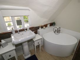 A bathroom with a white sink between two small tables and a white oval bathtub under a slanted ceiling at Church View in Welford-On-Avon