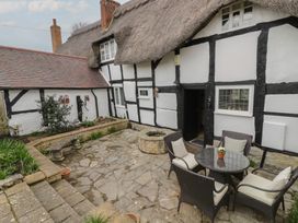 An outdoor patio with stone flooring a round table with four chairs a stone bench flowerbeds and a thatched roof cottage at Church View in Welford-On-Avon
